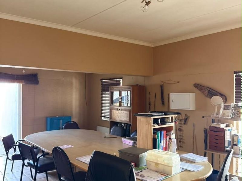 A spacious living area featuring tiled flooring, ceiling lighting, and sliding door access, currently utilized as a workspace with potential for renovation.