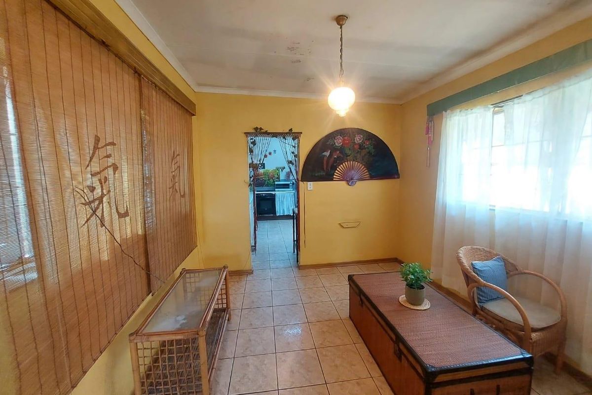 A living room featuring tiled flooring and a pendant light fixture, with visible ceiling water staining and dated wall finishes.