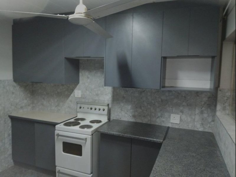 A functional kitchen featuring grey built-in cabinetry, stone-look tiled backsplash, laminate countertops, and a freestanding stove.