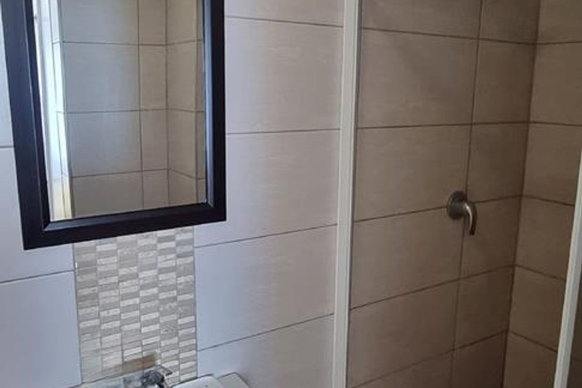 Modern bathroom featuring a wall-mounted basin, a glass-enclosed shower with tiled flooring, and decorative mosaic wall accents.