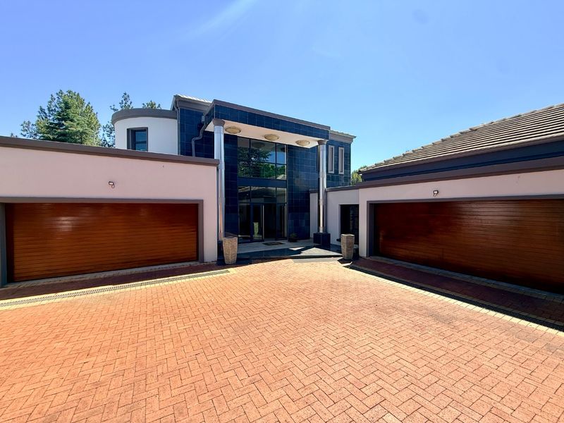 Modern front elevation featuring a paved driveway, double garage doors, and a striking glass entrance facade with metallic architectural columns.