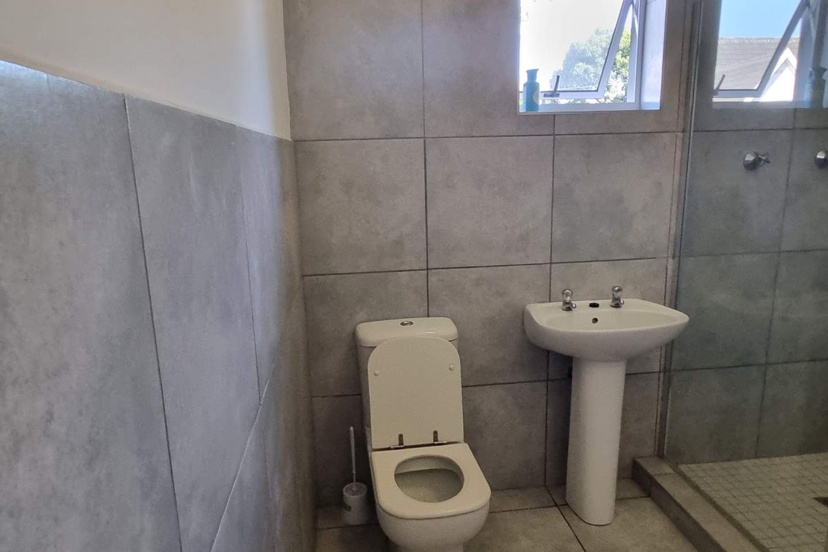 A modern bathroom featuring grey floor-to-ceiling wall tiles, a pedestal basin, a toilet, and a glass-enclosed shower area.