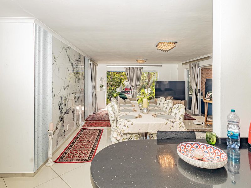 Spacious open-plan living and dining area featuring a modern kitchen island, marble-effect feature wall, and seamless access to the outdoor patio.