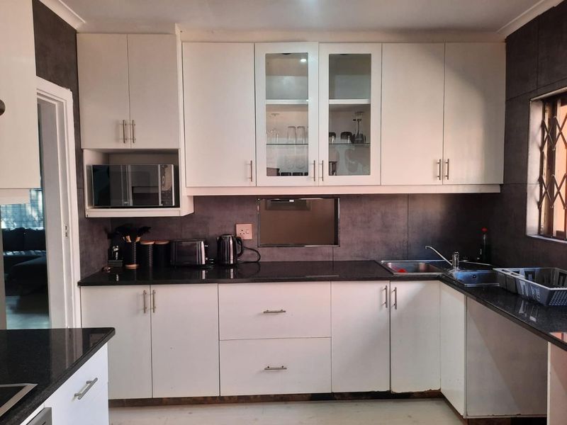 A functional kitchen featuring white cabinetry, dark granite countertops, a built-in microwave, and a tiled splashback with a stainless steel sink.