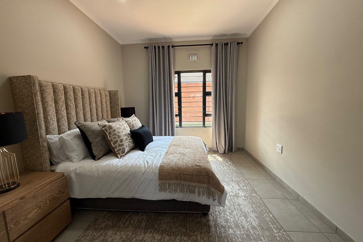 A well-maintained bedroom featuring neutral tiled flooring, recessed ceiling lighting, and a window with security bars and curtain tracks.