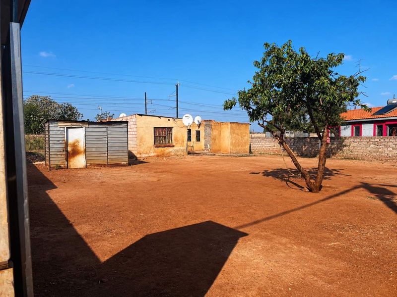 A spacious rear yard featuring a corrugated metal storage shed, a masonry boundary wall, and an unpaved ground area.