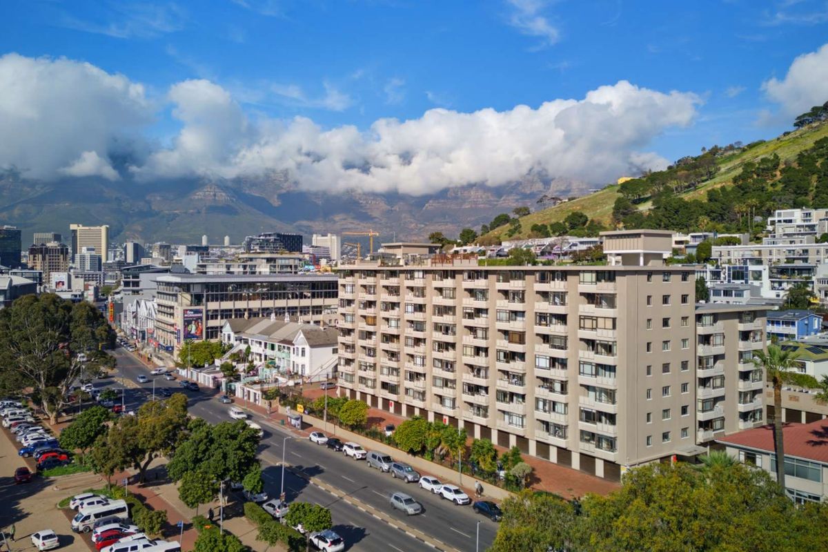 Aerial view of a multi-story apartment building situated in an urban environment with mountain views in the background.