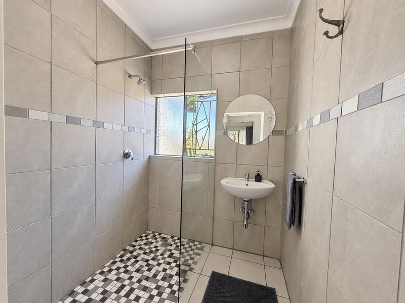 Modern bathroom featuring a walk-in shower with a glass screen, wall-mounted basin, and neutral tiled finishes throughout.