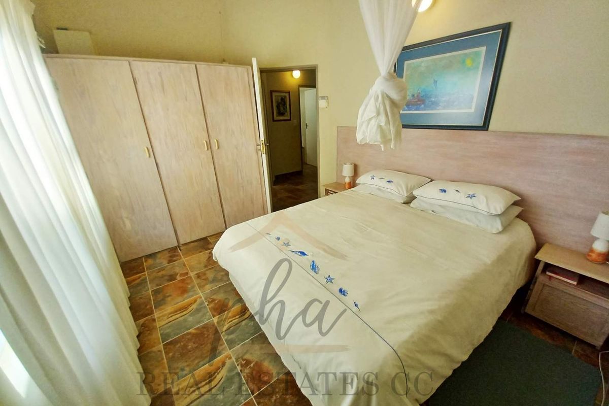 A bedroom featuring built-in wooden cupboards, tiled flooring, and a headboard, with an adjoining hallway visible.