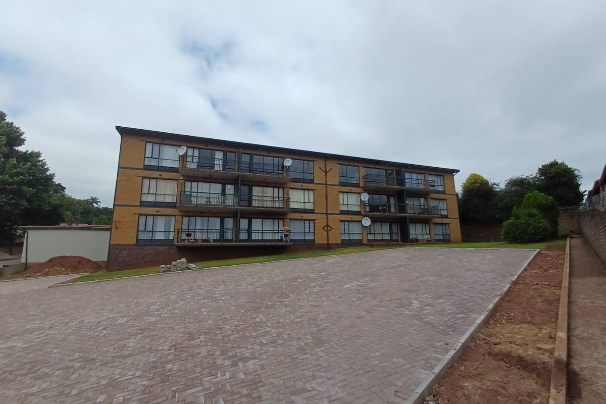 Rear view of a multi-story apartment building featuring brick facade, private balconies with metal railings, and a newly paved driveway area.