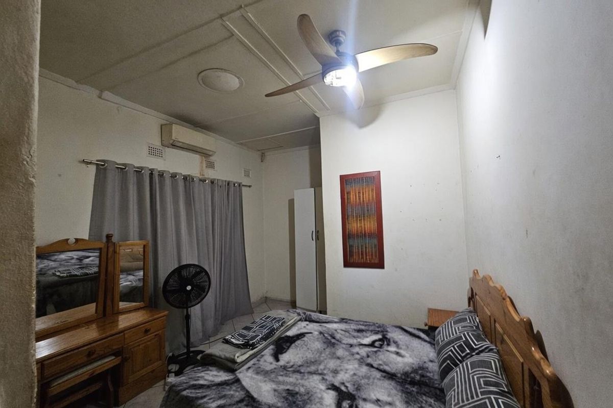A functional bedroom featuring a ceiling fan, wall-mounted air conditioning unit, and tiled flooring.