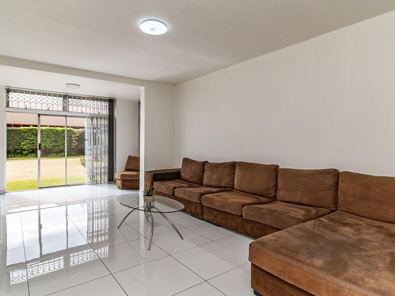 Spacious living room featuring polished white floor tiles, recessed lighting, and a large sliding glass door providing direct access to the rear garden.