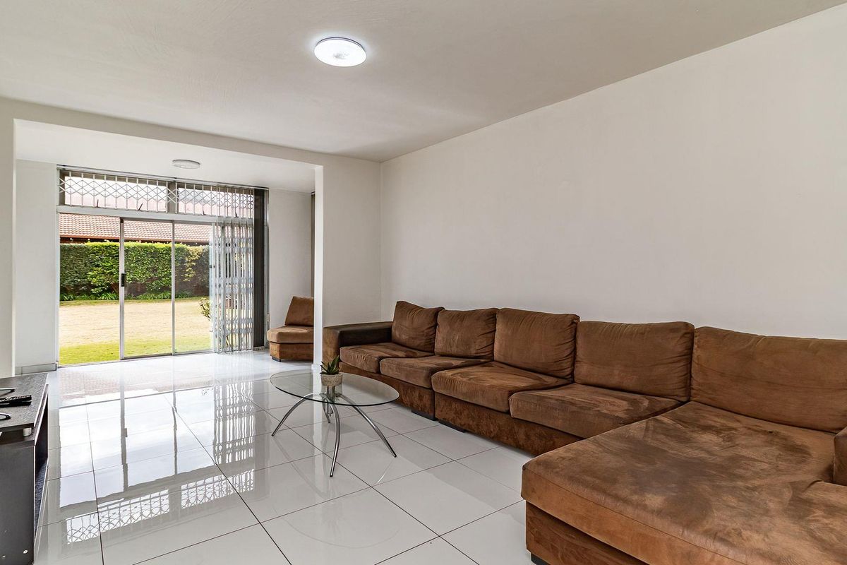 Spacious living room featuring polished white floor tiles, recessed lighting, and a large sliding glass door providing direct access to the rear garden.