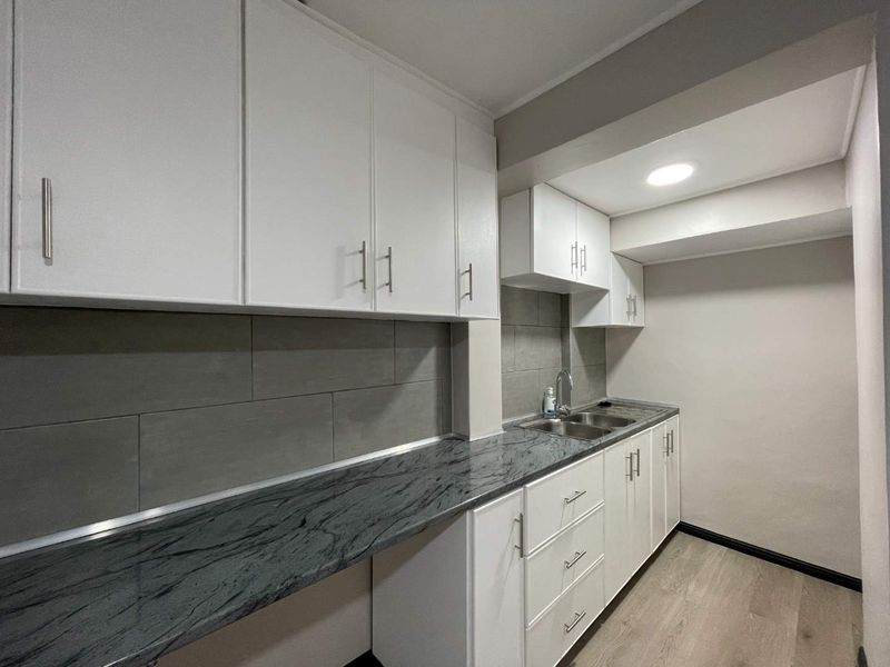 A clean, modern scullery featuring white cabinetry, dark stone countertops, a stainless steel sink, and grey tiled backsplash.