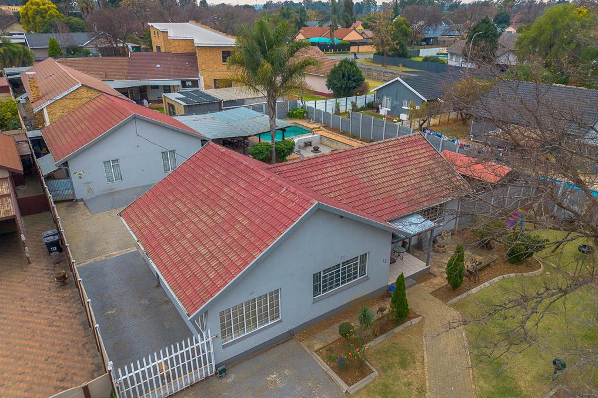 Aerial view of a residential property featuring a tiled roof, paved driveway, swimming pool, and established garden area.