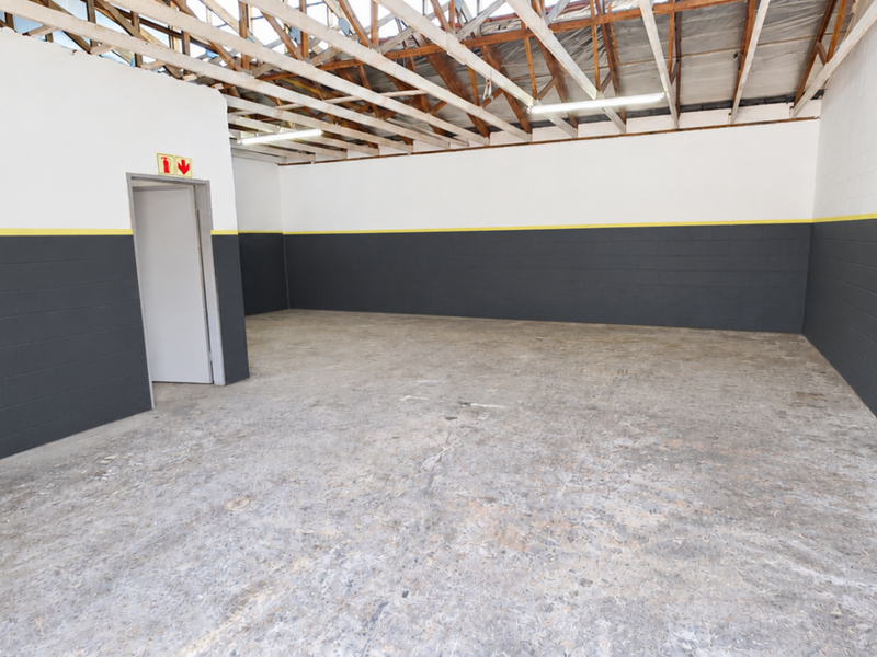 Spacious industrial utility area featuring exposed timber roof trusses, concrete flooring, and painted blockwork walls with a secure metal gate entrance.