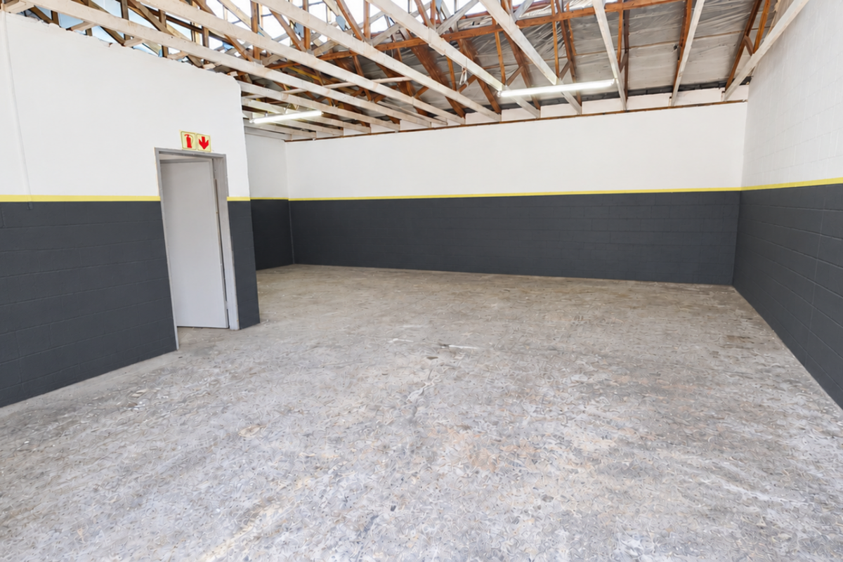 Spacious industrial utility area featuring exposed timber roof trusses, concrete flooring, and painted blockwork walls with a secure metal gate entrance.