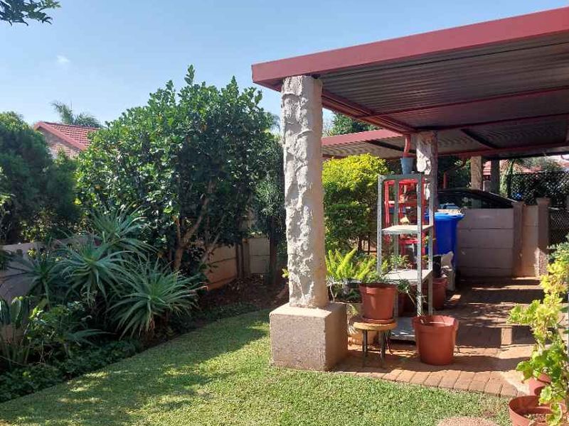 A covered patio area featuring a stone pillar, brick paving, and access to a private garden space.