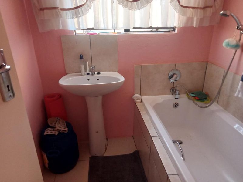 A compact bathroom featuring a pedestal washbasin and a built-in bathtub with a shower mixer, requiring cosmetic updates to modernize the space.