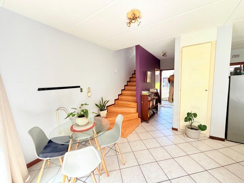Open plan living area featuring tiled flooring, a wooden staircase, and a built-in storage cupboard, providing a functional layout for the apartment.