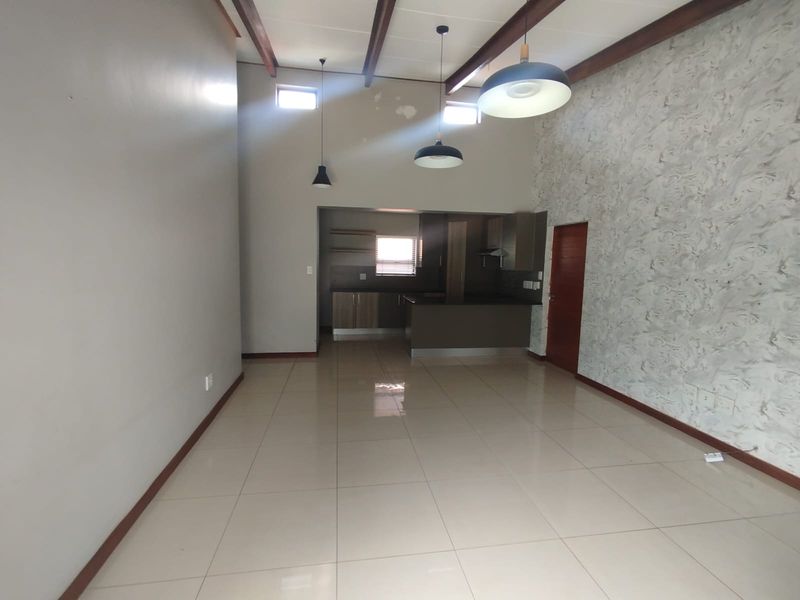 Spacious open-plan living and kitchen area featuring high ceilings with exposed timber beams, tiled flooring, and a modern kitchen with built-in cabinetry.