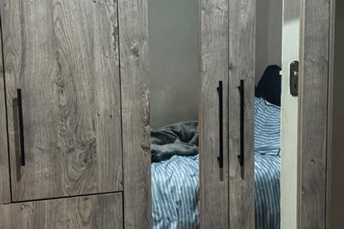 A bedroom featuring modern, full-height built-in wardrobes with a wood-grain finish, integrated mirror panels, and sleek black hardware.
