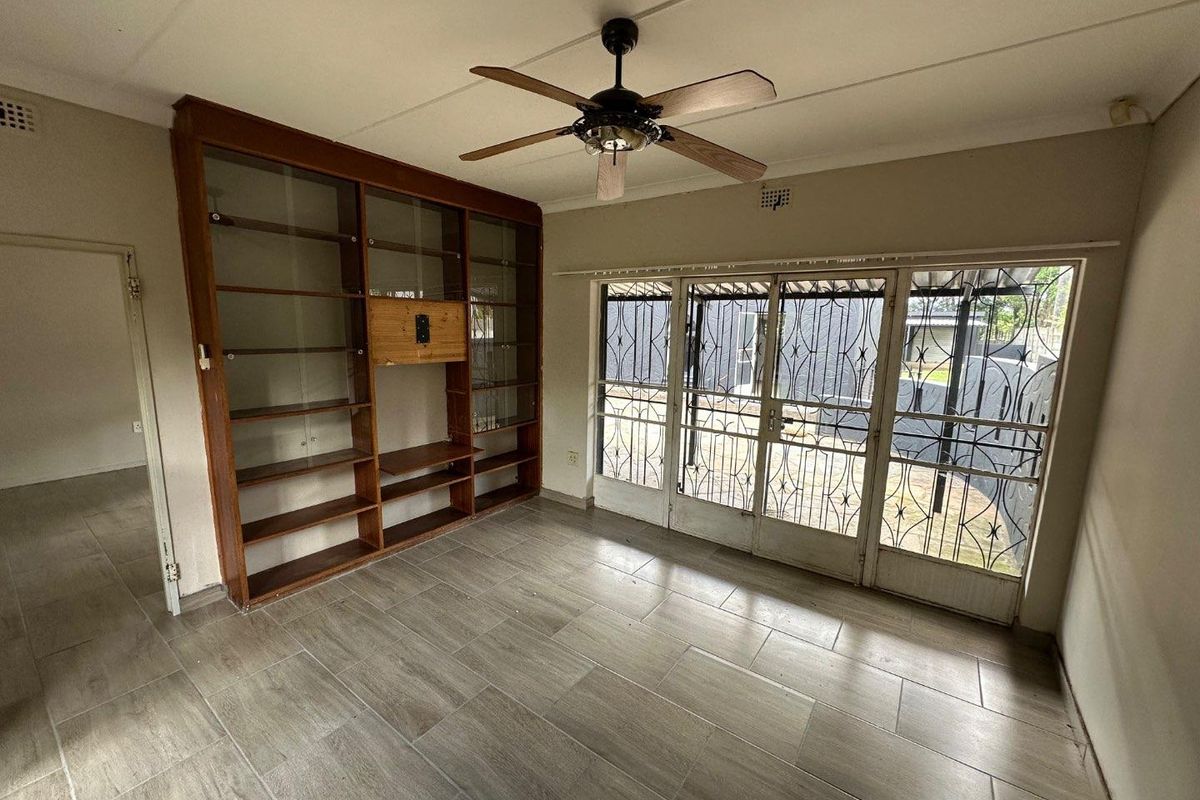 Living room featuring large built-in wooden shelving, tiled flooring, a ceiling fan, and sliding glass doors with security gates leading to the exterior.