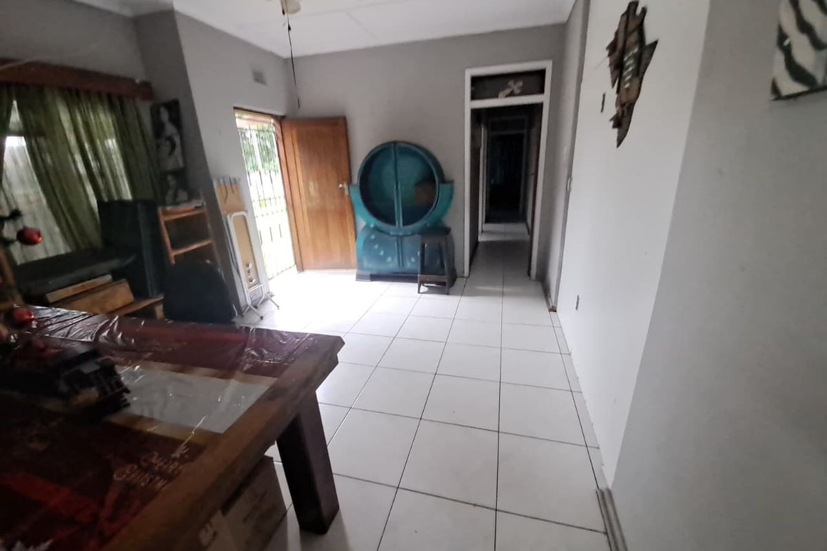 A living area featuring white tiled flooring, a ceiling fan, and direct access to an exterior doorway and hallway.