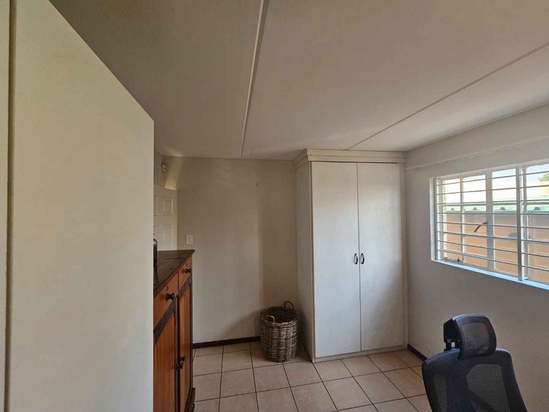 A bedroom featuring tiled flooring, a built-in wardrobe, and a window fitted with security bars.