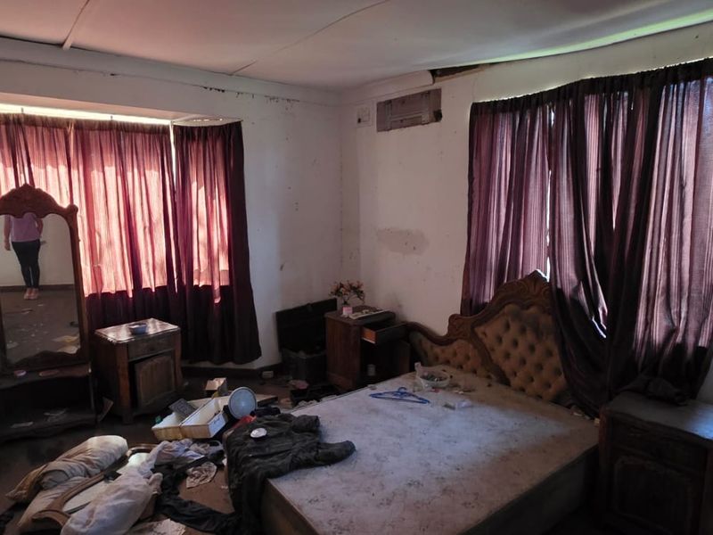 A bedroom featuring large windows with curtain rails and a wall-mounted air conditioning unit, requiring significant renovation and cosmetic repairs to the walls and ceiling.