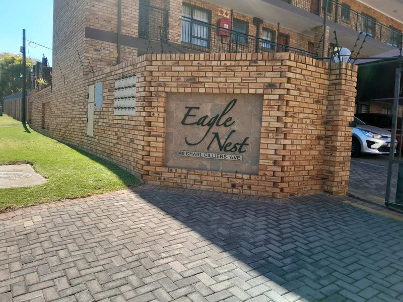 Front entrance view of the Eagle Nest apartment complex featuring a face brick boundary wall, paved driveway, and secure electric fencing.