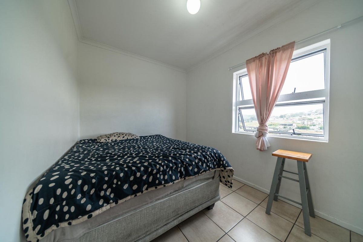 A functional bedroom featuring tiled flooring, neutral walls, and an aluminium window frame providing natural light and exterior views.