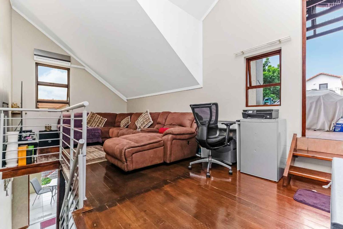 A loft-style living area featuring high vaulted ceilings, timber flooring, and direct access to an outdoor balcony space.