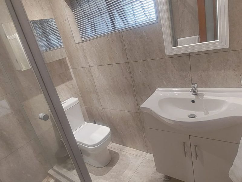 Modern bathroom featuring a glass shower enclosure, vanity cabinet with basin, toilet, and neutral floor-to-ceiling wall tiling.