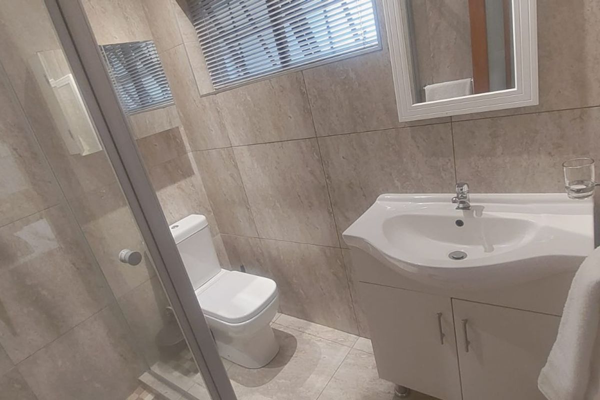 Modern bathroom featuring a glass shower enclosure, vanity cabinet with basin, toilet, and neutral floor-to-ceiling wall tiling.
