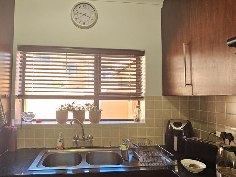 A functional kitchen area featuring dark wood-look cabinetry, a double bowl stainless steel sink, and a tiled splashback with natural light from the window.
