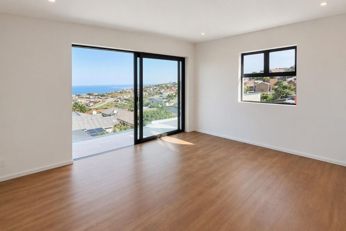 A bright, empty bedroom featuring modern laminate flooring, recessed lighting, and a large sliding glass door opening to a balcony with coastal views.