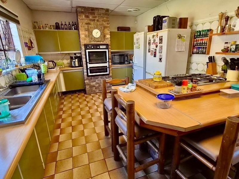 A functional kitchen featuring a brick chimney breast, built-in oven, gas hob, double sink, and ample cabinetry with a central breakfast nook area.