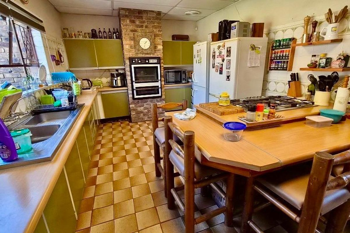 A functional kitchen featuring a brick chimney breast, built-in oven, gas hob, double sink, and ample cabinetry with a central breakfast nook area.