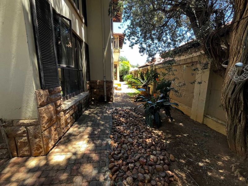 A side garden pathway featuring stone cladding on the building exterior, paved walkways, and established landscaping along the boundary wall.