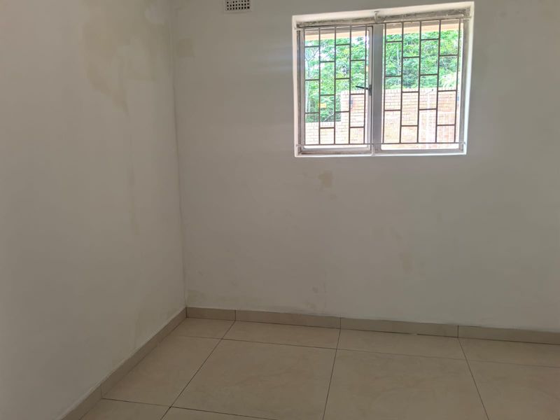 An empty bedroom featuring tiled flooring and a window with security bars, showing signs of wall staining and requiring cosmetic attention.