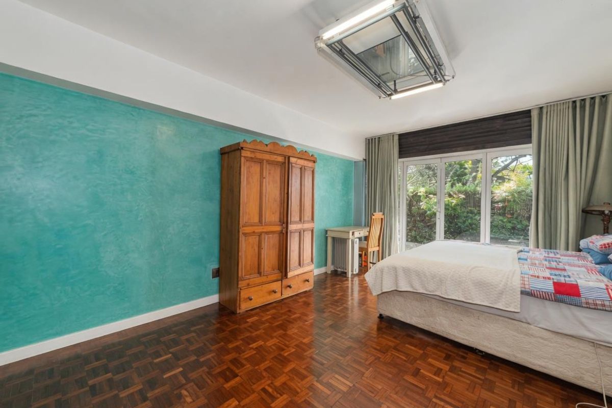 Spacious bedroom featuring classic parquet flooring, a vibrant accent wall, and large glass sliding doors providing direct access to the garden.