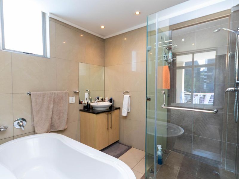 Modern bathroom featuring a freestanding bathtub, a separate glass-enclosed shower, and a vanity with a vessel sink, finished with neutral wall tiles.