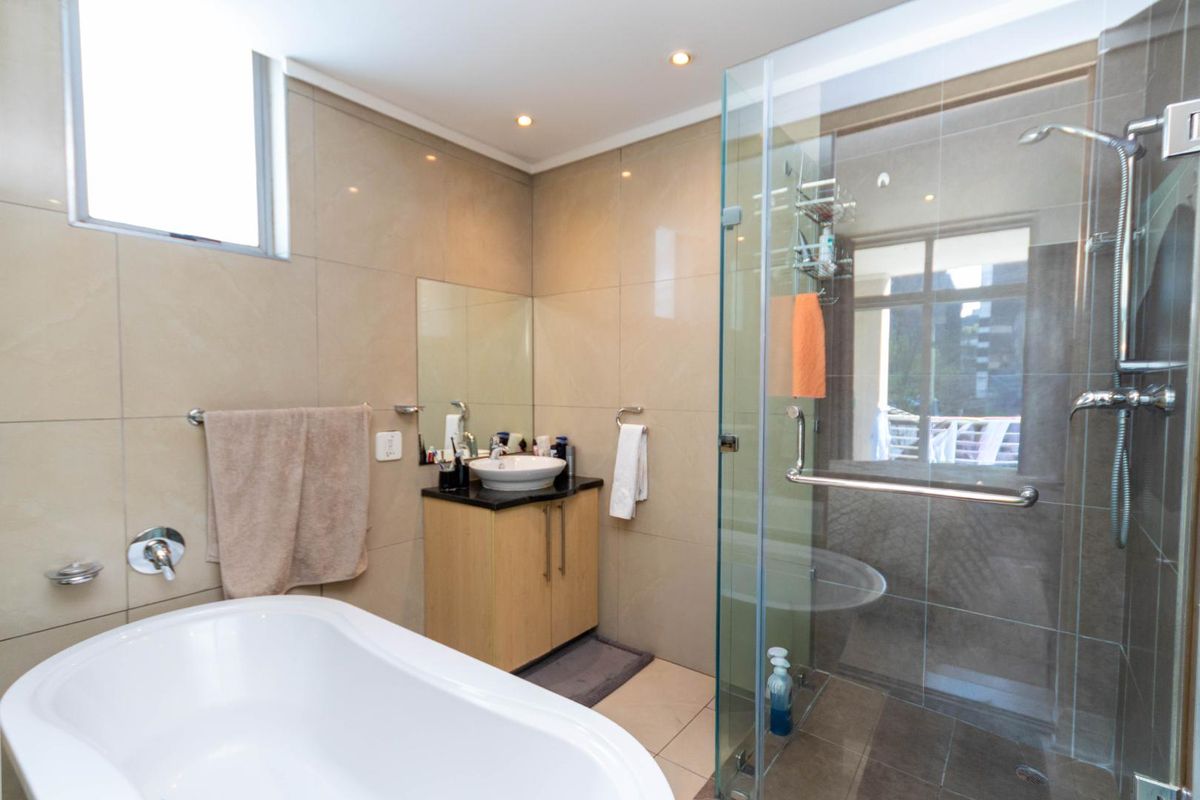 Modern bathroom featuring a freestanding bathtub, a separate glass-enclosed shower, and a vanity with a vessel sink, finished with neutral wall tiles.