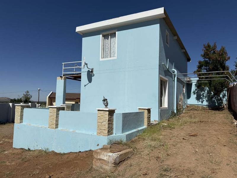 Rear view of a two-story house featuring a low boundary wall with stone-clad pillars, a small balcony, and an unlandscaped yard area.