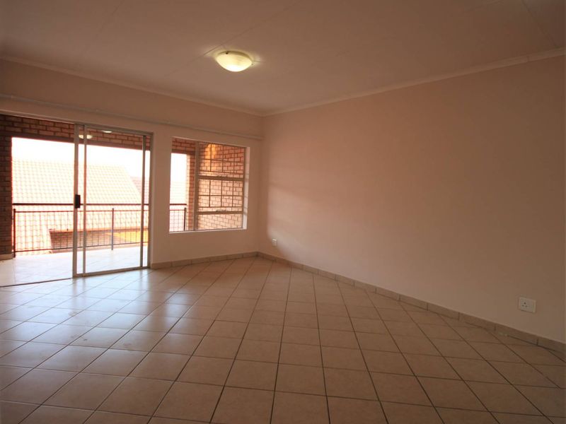 A bright, empty living room featuring neutral tiled flooring, a large window, and a sliding glass door providing access to an outdoor balcony area.