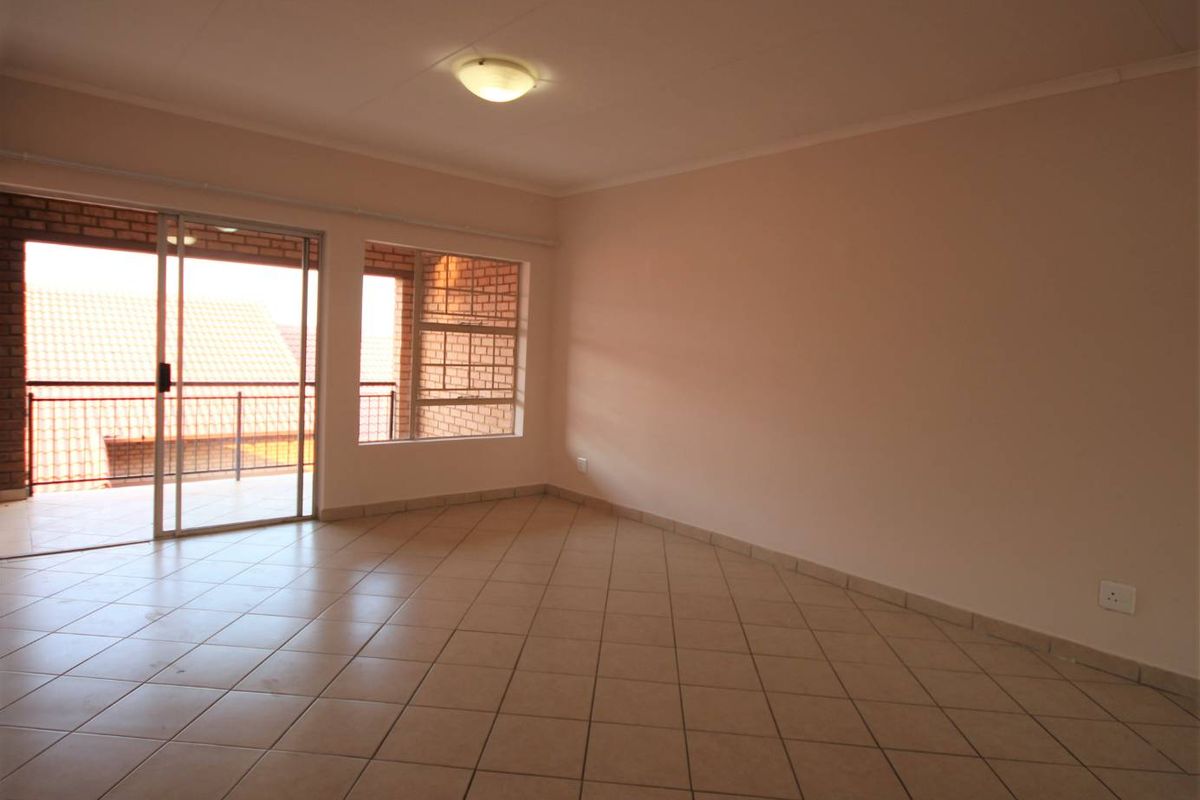 A bright, empty living room featuring neutral tiled flooring, a large window, and a sliding glass door providing access to an outdoor balcony area.