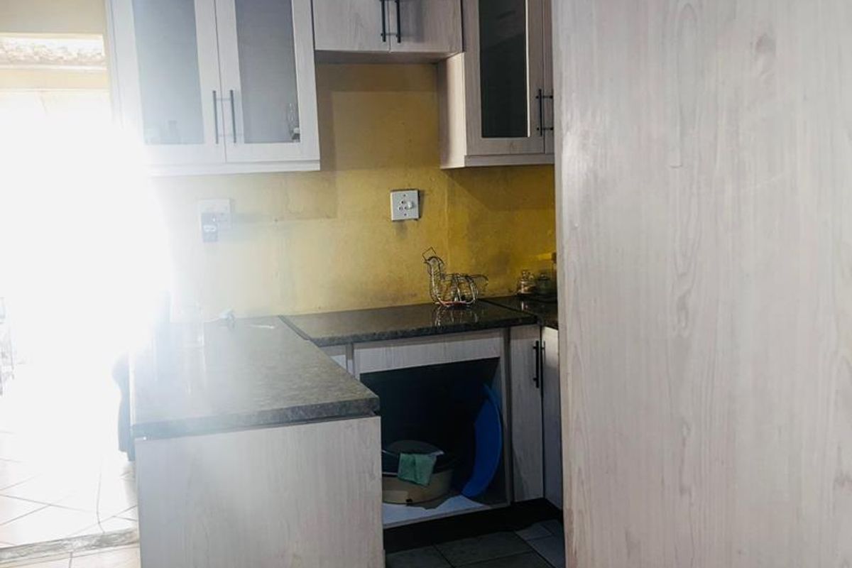 A compact kitchen featuring light wood-grain cabinetry, granite-look countertops, and tiled flooring, offering a functional layout with potential for cosmetic updates.