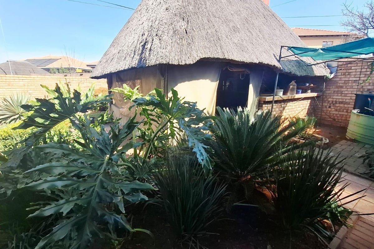 Rear garden area featuring a thatched lapa with a built-in bar counter, brick boundary walls, and established landscaping.