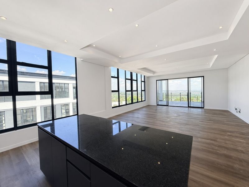 Spacious open-plan living area featuring a modern kitchen island with granite countertops, recessed lighting, and large windows leading to a private balcony.
